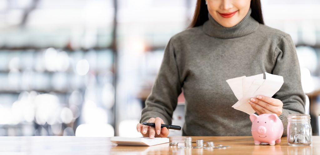 Mujer calculando finanzas con recibos, calculadora y alcancía, representando la importancia del CFDI en la compraventa de inmuebles en México.