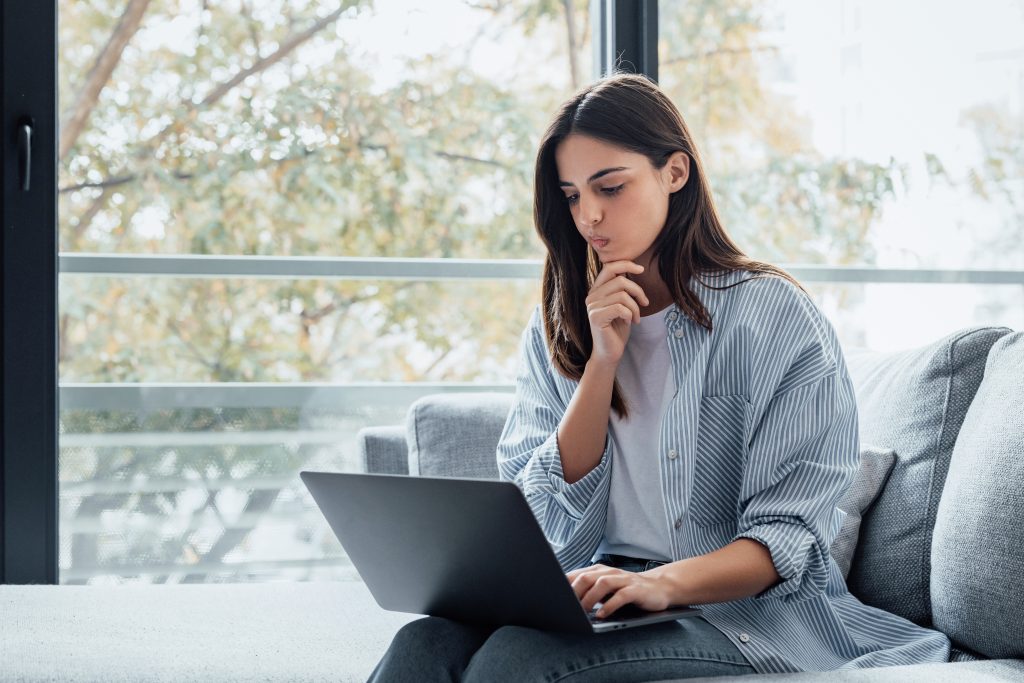 Mujer joven consulta su laptop en casa mientras analiza información financiera sobre el buró de crédito y el pago de predial en Mexicali