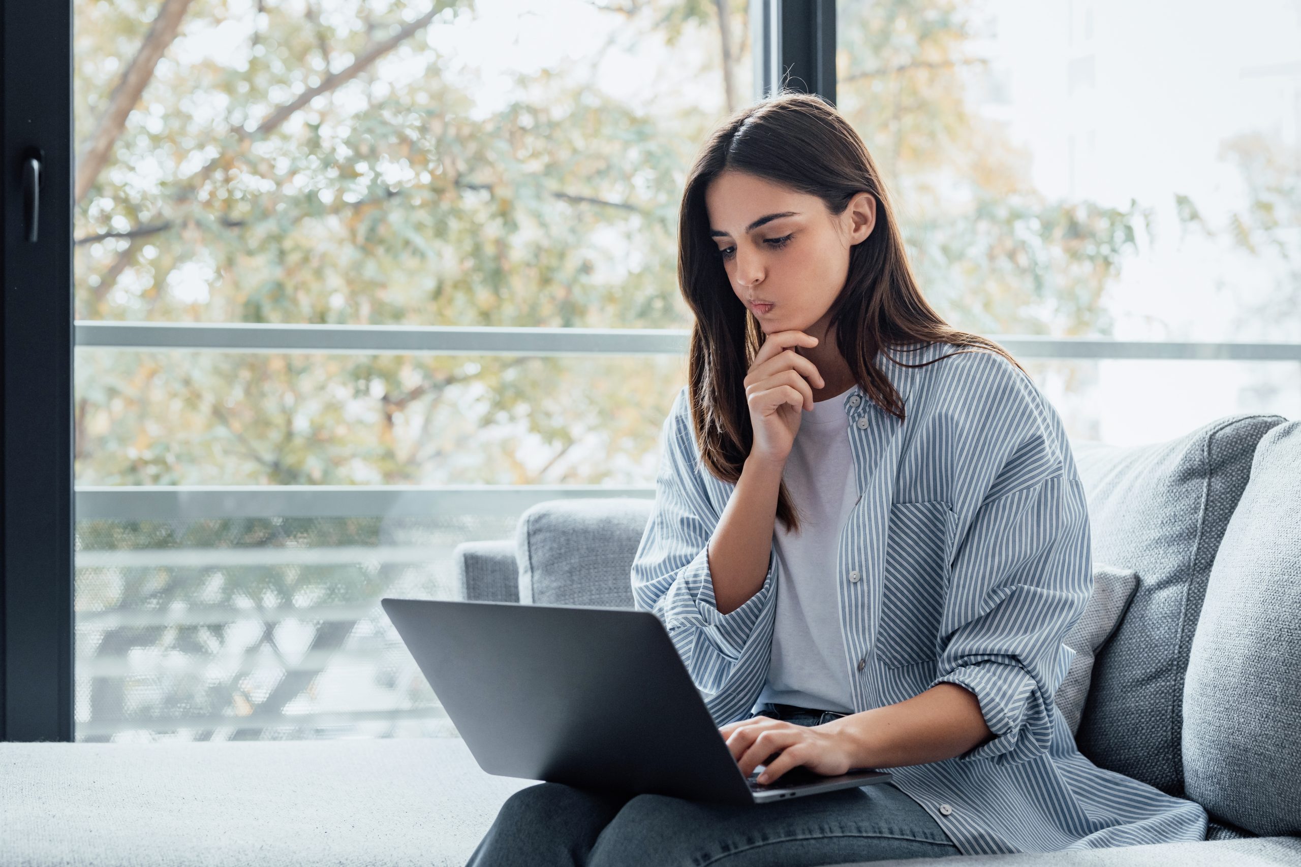 Mujer joven consulta su laptop en casa mientras analiza información financiera sobre el buró de crédito y el pago de predial en Mexicali
